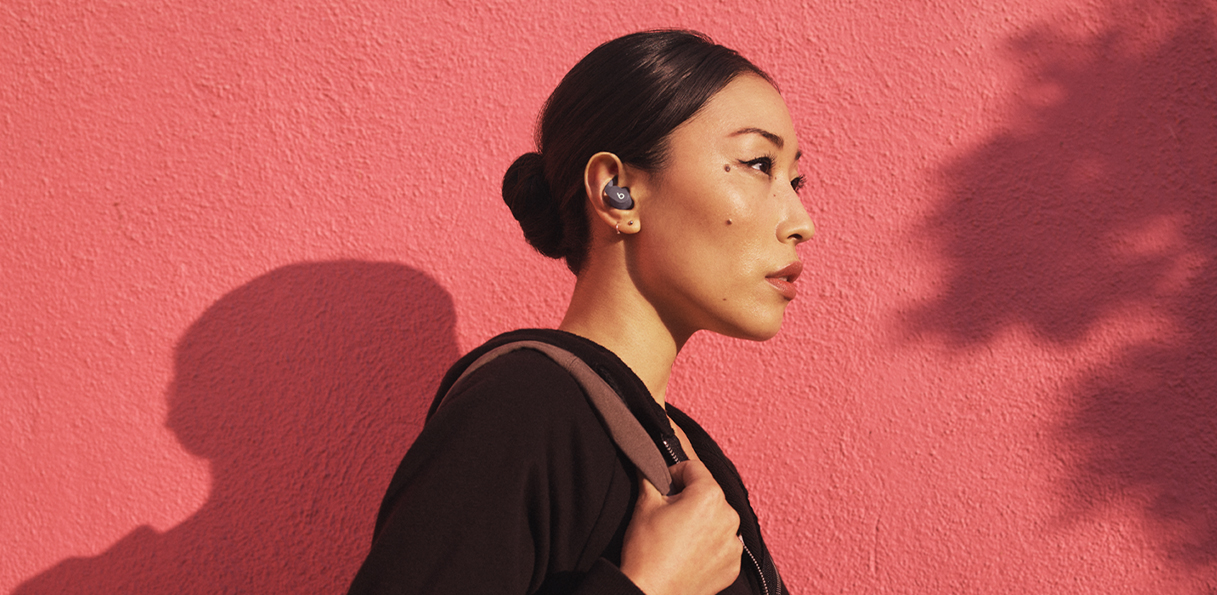 佩戴 Beats Fit Pro 的亚裔女性在红墙前往外走